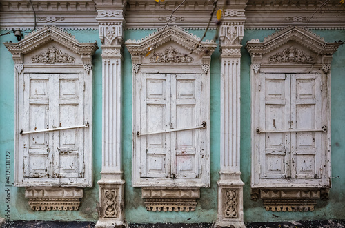 Three windows with closed shutters of an old house with carved decor and stucco, a fragment of the facade. Russia, city of Orenburg