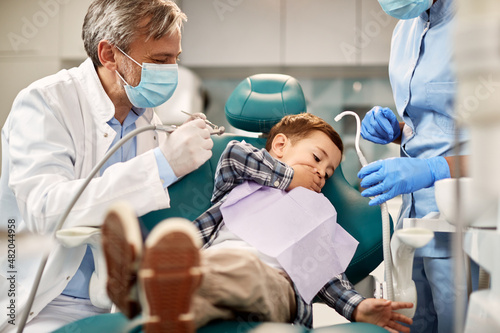 Scared little boy refuses to open his mouth during dental exam at dentist's office.