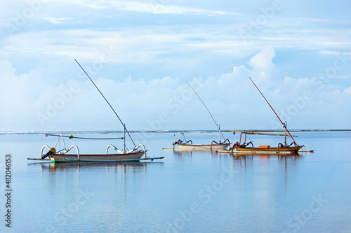 Fishing boats floating on the ocean. Wooden boat sailing in open waters. Sailing boat landscape. High waves with foam spread on the coast. Tropical landscape. Bali island, Indonesia. Summer vacation.