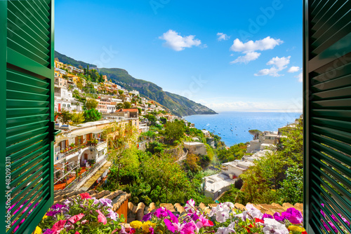 Mountain, city and sea view through an open window with shutters of the city of Positano on the Amalfi Coast of Southern Italy during summer.