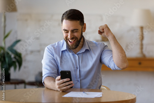 Happy excited smartphone user enjoying win, success, achieve, high job result. Euphoric businessman using cellphone, reading text message, feeling joy, making hand winner gesture, laughing