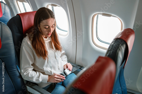 Young woman fastening seatbelt in passenger airplane