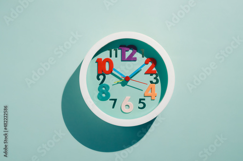 Photos of round children's wall clocks with multi-colored numbers on blue background with shade. Top View. Cheerful watch with multi-colored dial. flat lay