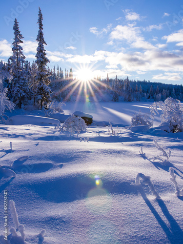 The sun shining at a low angle directly into the lens, creating a lens flare. Snowy landscape by the lake, Norwegian mountain