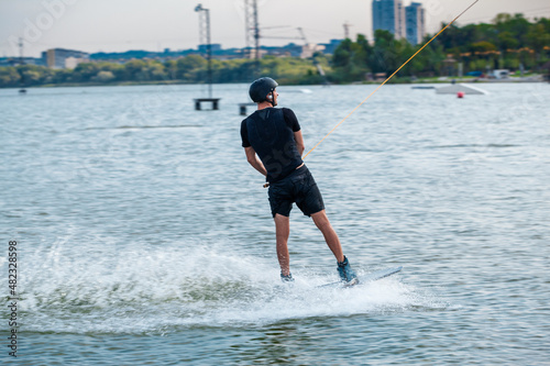 Rear view of wakeboarder sliding on water of city river holding on to towing rope