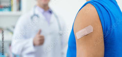Plaster on arm of man and thumb up of doctor after third vaccination against Covid 19