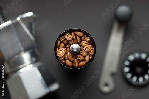 Coffee grinder with coffee beans and coffee maker on gray background top view. Beans in focus, coffee setup with background blurred.