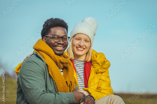 Young beautiful couple blonde girl in warm clothes and man in white t-shirt having fun in the grass in a field in nature at sunset. Happy young loving couple sitting, laughing and hugging