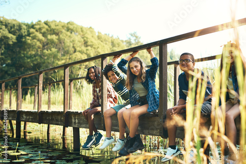 Life is sweet up the creek. Shot of a group of teenagers sitting on a bridge in nature at summer camp.