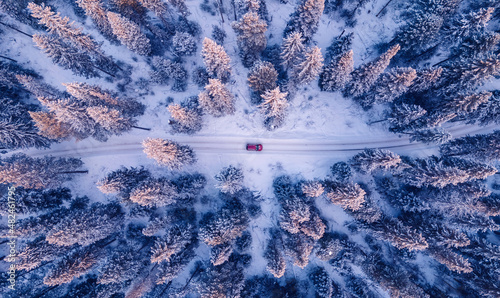 Red car driving on winding road through snowy forest, toning blue. Concept banner winter travel, aerial view