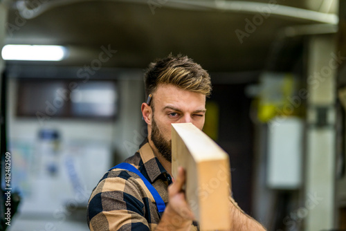 Young handsome caucasian carpenter checking the wooden board in old way