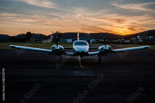 Avião bimotor de transporte aéreo de poucas pessoas, além do piloto. Avião estacionado ao crepúsculo vespertino. 