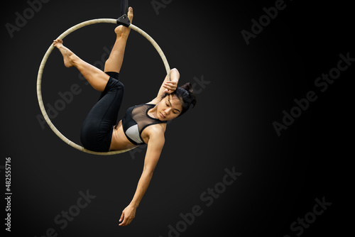 Young Asian gymnast woman doing gymnastics performance on aerial hoop in fitness gym. Female acrobat posing on aerial ring.