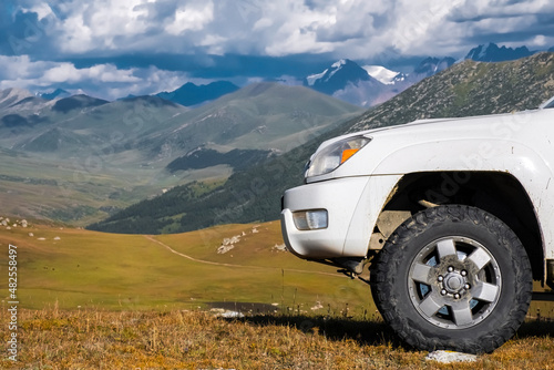 White SUV on mountain rocky valley with mountains and cloudy sky background.