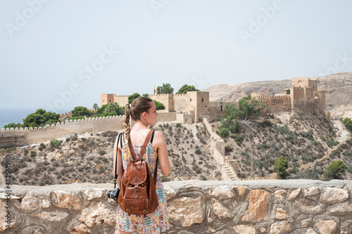 Young traveler girl with leather backpack and camera at the viewpoint of the Alcazaba