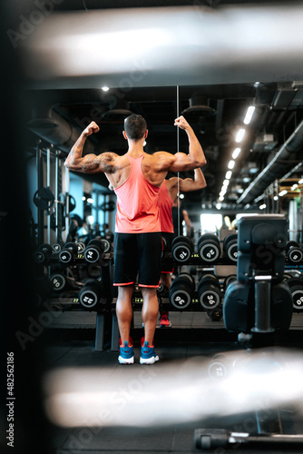 Portrait of smiling muscular athletic man working out biceps and triceps using dumbbells, lifting weights at gym. Athlete and professional certified trainer training with weights at gym.