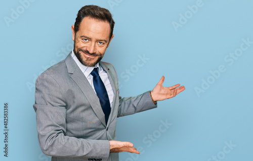 Middle age man wearing business clothes inviting to enter smiling natural with open hand