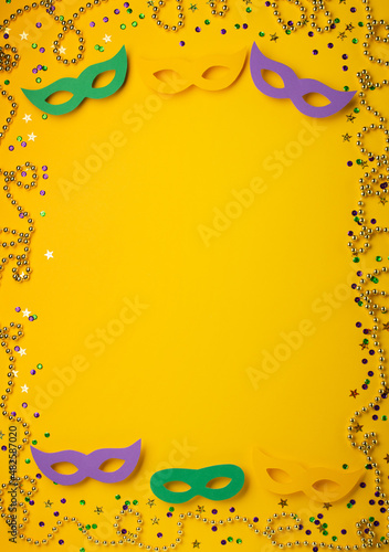 Mardi Gras gold color beads with Masquerade festival carnival masks and golden, green, purple confetti on yellow background.