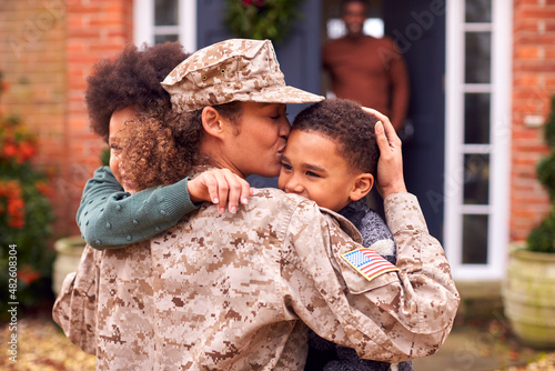 American Female Soldier In Uniform Returning Home To Family On Hugging Children Outside House