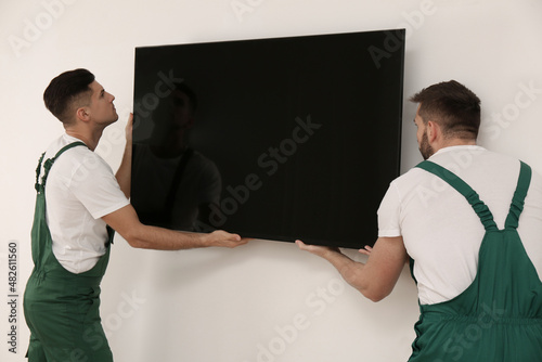 Professional technicians installing modern flat screen TV on wall indoors