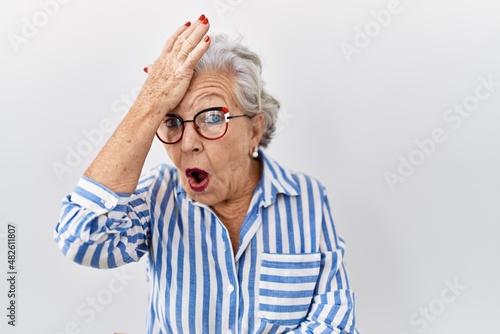 Senior woman with grey hair standing over white background surprised with hand on head for mistake, remember error. forgot, bad memory concept.