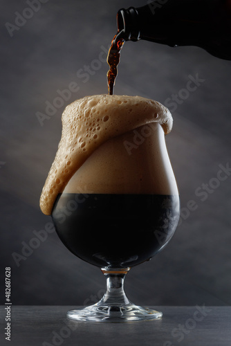 Stream of dark stout pours into a beer glass. Detail of dark beer with overflowing foam head. Selective focus 