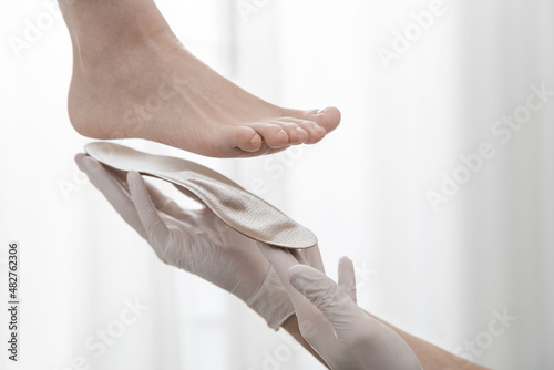 Orthopedic insole on a white background. Hands in rubber gloves hold an orthopedic insole. Foot care, comfort for the feet. Doctor orthopedist tests the medical device. Flat feet correction.