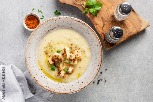 Cauliflower cream soup with croutons in a bowl on grey concrete table background, top view