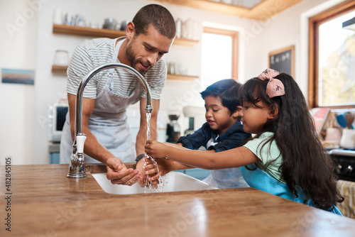 Let's wash those germs away. Cropped shot of a man and his two children washing their hands in the kitchen basin.