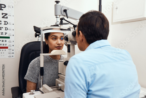 Can't see Come to me. Shot of a young woman getting her eyes examined with a slit lamp by an optometrist.