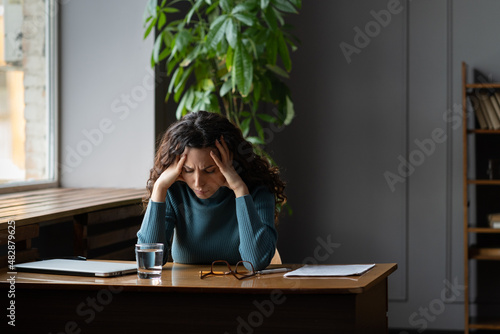 Exhausted stressed woman sitting at office desk with closed laptop tired of overwork, stress, problems and lack of inspiration. Female writer or student suffer from professional burnout at workplace