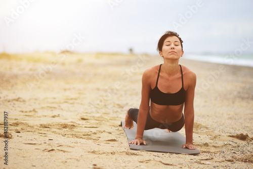 A portrait of beautiful woman standing in plank position and stretching her back on the beach. Yoga sport. Healthy wellness lifestyle. Spiritual health. Personal fulfillment.