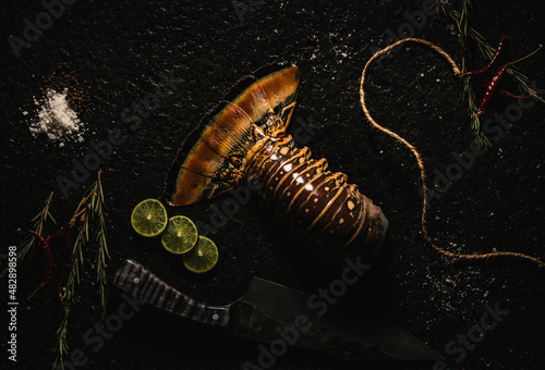  LANGOSTA sobre laja de piedra con decoración como sal, pimienta limón, chile de árbol , romero y un cuchillo 