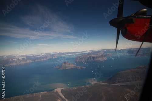 wybrzeże grenlandii z dużej wysokości i śmigło małego czerwonego samolotu widziane przez okno kabiny pilota