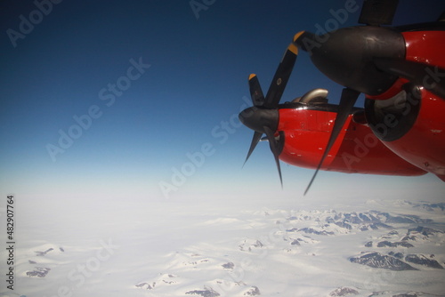 wybrzeże grenlandii z dużej wysokości i śmigło małego czerwonego samolotu widziane przez okno kabiny pilota