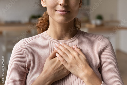 Close up cropped view young attractive Hispanic woman stand alone indoor put folded palms on chest feeling grateful and appreciation, express sincere feelings. Believe, charity, body language concept