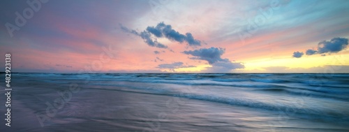 Baltic sea at sunset. Dramatic sky, glowing clouds, soft golden sunlight. Waves, splashing water. Picturesque dreamlike seascape, cloudscape. Panoramic view, long exposure. Nature, weather themes