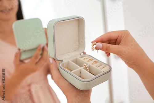Young woman taking earring from jewelry box near mirror