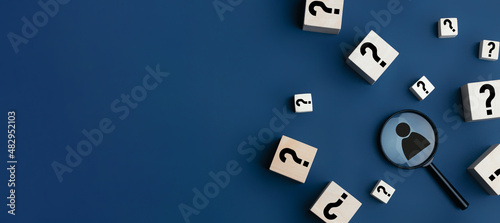 Concept of finding a creative idea or solving a problem. Question mark on wooden cubes and a magnifying glass with a human icon on a blue background.