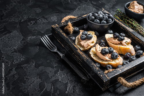 Foie gras toasts, duck liver pate and fresh blueberry in wooden tray. Black background. Top view. Copy space