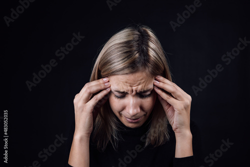 Portrait of crying woman with face down hand fingers touching temples on black background. Victim of physical and psychological abuse. Gaslighting. Relative aggression.
