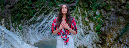 Young woman in white dress and plaid shirt practicing breathing yoga pranayama outdoors in moss gorge. Unity with nature concept.