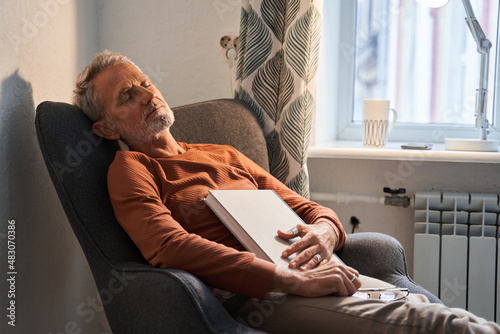 Tired mature man sleeping at the armchair with book on chest after reading