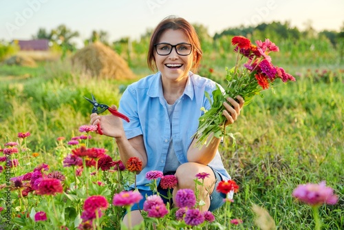 Smiling middle aged female holding bouquet of fresh zinnia flowers in garden