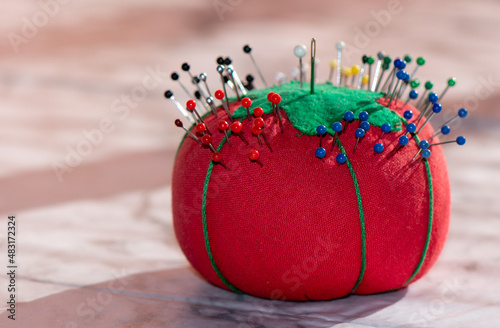 Red pincushion holding many multi-colored bead-head pins