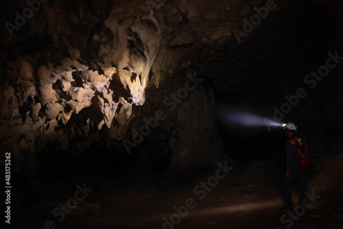 A male speleologist with helmet studying the walls of the dark cave