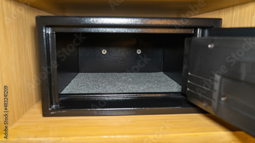 An open black empty safe with its door open in a wooden shelf.