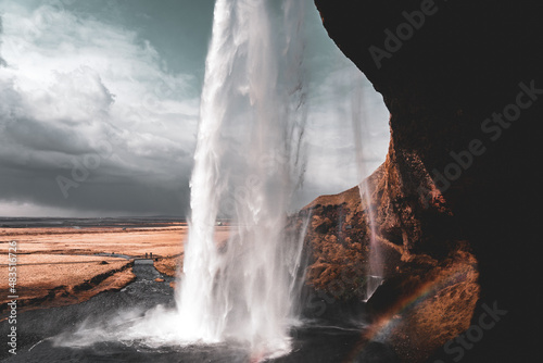 View of Seljalandsfoss from behind waterfall with a rainbow forming in Iceland