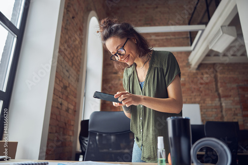 Smiling woman, interior designer or architect taking photo of a blueprint using smartphone, working on new project, standing in her office