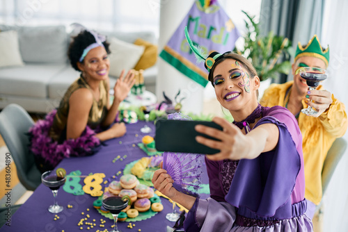 Group of cheerful friends in carnival costumes celebrate Mardi Gras and take selfie with smart phone.